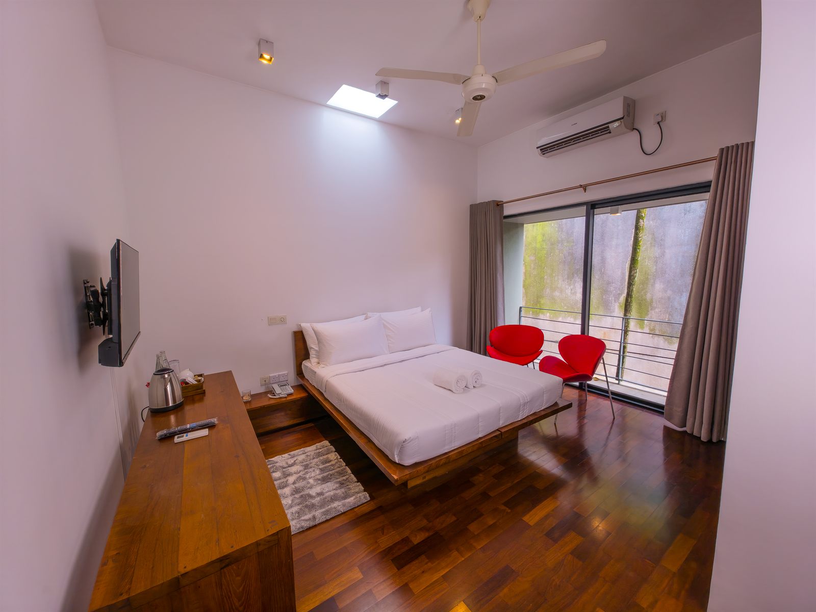 Deluxe Room with bed, TV, balcony window, and red chairs