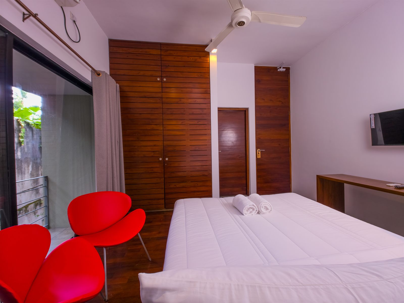 Deluxe Room bed, red chairs, TV, and wooden wardrobe